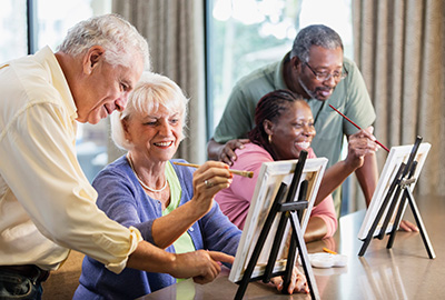 Two multi-ethnic women sitting at a table indoors, painting on small canvases.