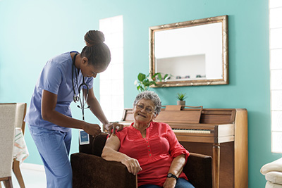 A female home caregiver giving a medical shot to a senior woman sitting on an armchair at home.